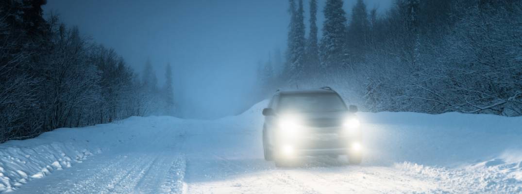 Vehicle driving through snow with headlights on.