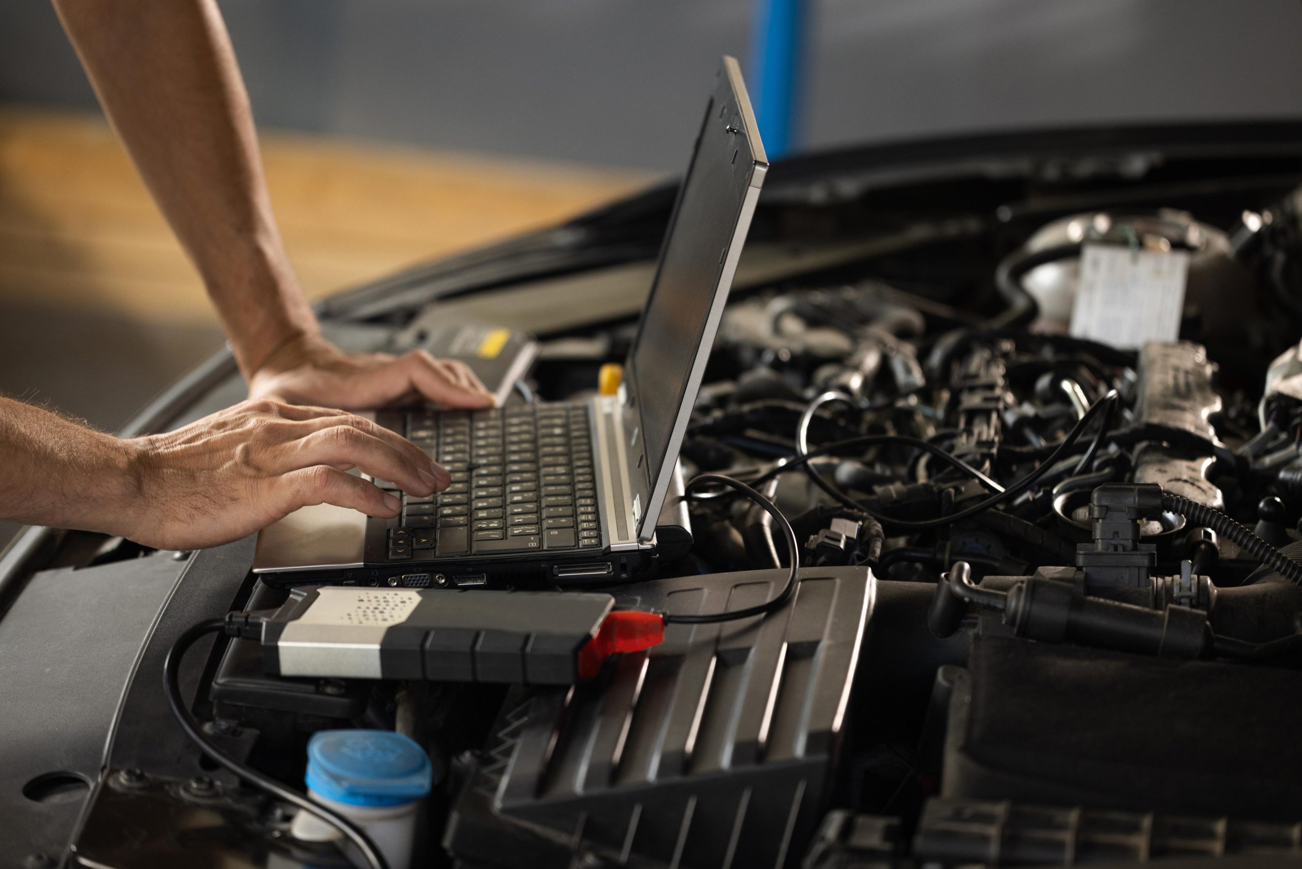 Tech working on a laptop with vehicle hood open